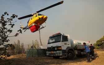 epa11546315 A helicopter fills up its container with water during a wildfire in Penteli, northeast Attica, Greece, 12 August 2024. Despite efforts by civil protection forces throughout the night, the fire raging in northeast Attica had advanced rapidly and was moving in the direction of Penteli, having spread over the Penteli mountain range. Authorities evacuated the Penteli Children's Hospital and the 414 Military Hospital in the area.  EPA/GEORGE VITSARAS