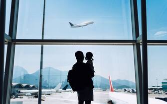Silhouette of joyful young Asian father carrying cute little daughter looking at airplane through window at the airport while waiting for departure