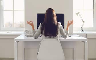 Back view. Business woman brunette meditates at the workplace at the table in the office.