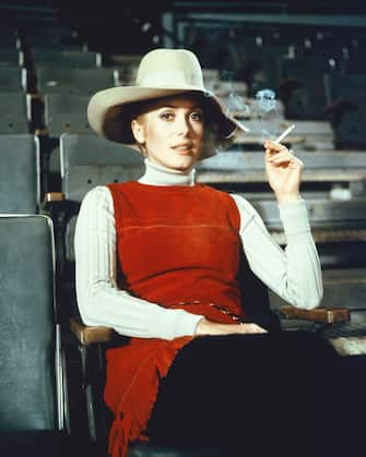 Catherine Deneuve, French actress, smoking a cigarette while wearing a wide-brimmed hat, a red sleeveless top and a white polo neck jumper, in a publicity portrait issued for the film, 'The April Fools', 1969. The 1969 romantic comedy, directed by Stuart Rosenberg (1927-2007), starred Deneuve as 'Catherine Gunther'. (Photo by Silver Screen Collection/Getty Images)