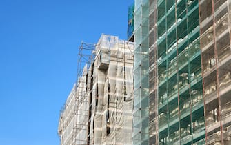 Works for adaptation and energy saving of buildings in Italy. Low angle view of two tall building with scaffolding in front of the facades.