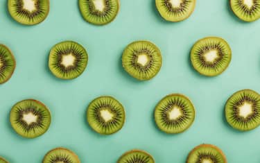 The patterns of the slices of kiwi fruit on green background as a continuous background. Textured conceptual fruit background