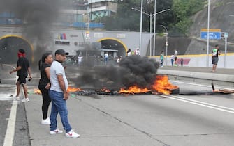 epa11507534 People look at a road blocked by burnt tires during a demonstration following presidential election results in the primero de Mayo sector in Caracas, Venezuela, 29 July 2024. According to the first report from the National Electoral Council (CNE), Maduro was re-elected for a third consecutive term in the elections held on 28 July, in which he obtained 51.2 percent of the votes (5,150,092 votes), while the standard-bearer of the majority opposition, Edmundo Gonzalez Urrutia, obtained 4,445,978 votes, which represents 44.2 percent of the votes. The opposition is calling for the release of the full vote count.  EPA/Manuel Diaz