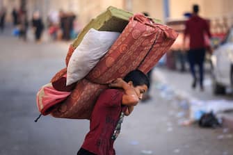TOPSHOT - A boy carries a mattres as Palestinians with their belongings flee to safer areas in Gaza City after Israeli air strikes, on October 13, 2023. Israel has called for the immediate relocation of 1.1 million people in Gaza amid its massive bombardment in retaliation for Hamas's attacks, with the United Nations warning of "devastating" consequences. (Photo by MAHMUD HAMS / AFP) (Photo by MAHMUD HAMS/AFP via Getty Images)