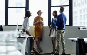 Cheerful multi-ethnic business people standing by office window during coffee break