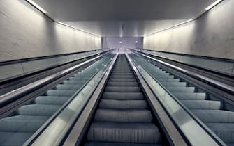 Modern and new interior with the muted colours of the glass and metal escalators with gray concrete walls. It is futuristic and efficient looking. There are no people.