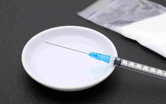 Drug injection syringe and melted heroin with bag on black table