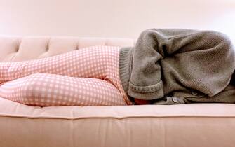 mid adult woman clutches stomach while lying down on couch