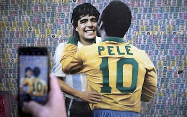 A man takes a picture of a wall depicting an image of late football stars Diego Maradona of Argentina and Pele of Brazil embracing each other, in Buenos Aires on December 29, 2022, just hours after the passing of Pele. (Photo by Juan MABROMATA / AFP)
