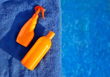 Cosmetic sunscreen products, set different orange bottles of sun protection body cream on blue towel against swimming pool. Skin care and protection
