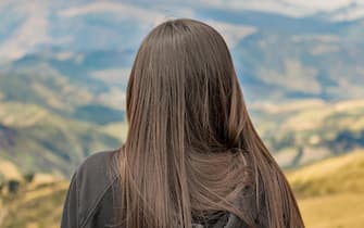 Back view of adult young woman with black straight hair contemplating the landscape of andes range in Quito, Ecuador