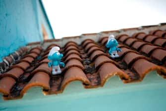 Two Smurfs are pictured on a roof of a house in Juzcar during the shooting of the Smurfs 3D on June 16, 2011 in Juzcar near Malaga, Southern Spain. The movie on animated, blue colored and elf-like characters called Smurfs designed by Belgian cartoonist Peyo will have the world premiere in the village of Juzcar. The facades of the houses of Juzcar have been painted blue after Sony chose it for the world premiere of the new movie 'The Smurfs 3D'. AFP PHOTO / JORGE GUERRERO (Photo by Jorge Guerrero / AFP) (Photo by JORGE GUERRERO/AFP via Getty Images)