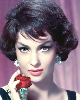 Headshot of Gina Lollobrigida, Italian actress, wearing pearl earrings and holding a red rose to her chin in a studio portrait, circa 1955. (Photo by Silver Screen Collection/Getty Images)