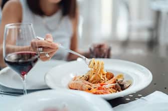 Mid-section of young woman eating seafood pasta and having wine, sitting at an outdoor Italian restaurant during vacation. Luxury meal. Travelling for good food.