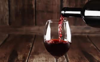 Red wine is poured to glass on wooden background