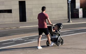 Rear view of a father pushing a stroller with his baby  inside in a street at summer.