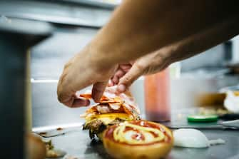 Close up of a middle aged Chef preparing a cheeseburger with his hands in a professional kitchen