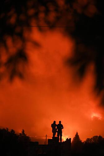 epa10812674 Two men watch the wildfire in Avantas village, near the city of Alexandroupolis, Thrace, northern Greece, 21 August 2023. The wildfire that broke out early on 19 August in a forest in the Melia area of Alexandroupolis has spread rapidly due to the strong winds blowing in the area and is raging uncontrolled. The major wildfire in Alexandroupolis continues with unabated intensity for the third consecutive day. According to the Fire Department, the fire is difficult to be contained due to the strong winds in the area.  EPA/DIMITRIS ALEXOUDIS