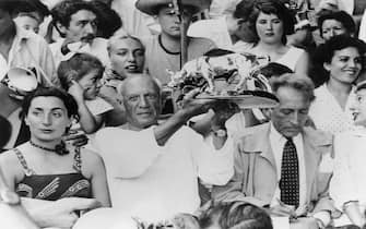 Spanish-born artist Pablo Picasso (1881 - 1973) holds up a statuette of a fighting bull, presented to him by toreadors in appreciation of his art, in the stands at a bullfight at Vallauris, France, 11th August 1955. On the left is Jacqueline Roque (1927 - 1986), who later married Picasso. On the right is French author, artist and filmmaker Jean Cocteau (1889 - 1963). (Photo by Keystone/Hulton Archive/Getty Images) 