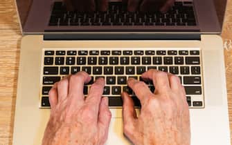 Senior adult man touch types on laptop