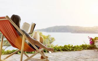 Woman reading book while relaxing on deck chair at back yard