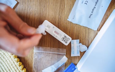 A woman squeezing the sample liquid on a test strip while carrying out a Covid-19 rapid self test at home.