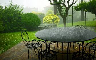 Pouring rain on wrought iron weather-resistant  garden furniture, round table and elegant chairs.