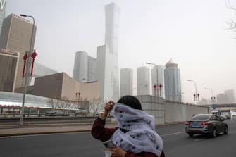 A pedestrian covers her face with a scarf while walking along a road shrouded in smog during a sandstorm in Beijing, China, on Wednesday, March 22, 2023. Beijing warned vulnerable residents to stay indoors Wednesday, as a sandstorm  the third this month  combined with regular industrial pollution to create a thick, unbreathable haze over the city, the worst inÂ two years.Â Source: Bloomberg