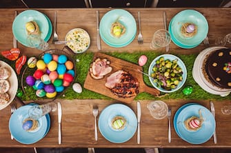 Decorated table for Easter celebration. On the table is glazed ham,painted eggs,tulips and Easter cake. top-down composition