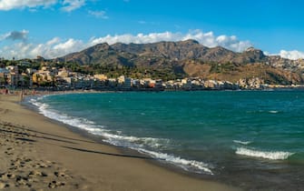 View of Taormina and Castelmola viewed from beach at Giardini Naxos, Sicily, Italy, Mediterranean, Europe