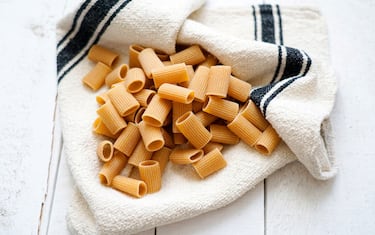 Raw whole wheat pasta Mezze Maniche on white wooden background, Italy, Europe
