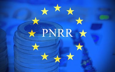 Close up of a stack of 1 euro coins with euro banknotes and European flag as background with the text "PNRR" .