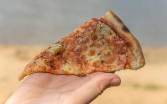 Fast food, female hand holding a slice of pizza, on the beach.