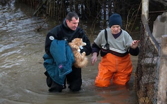 A rescuer carries a cat and helps a woman during an evacuation of residents of the flooded village of Pribrezhnoe in Crimea on November 27, 2023, following a storm. Over 400,000 people in Crimea were left without power on November 27, 2023 after hurricane force winds and heavy rains battered the Russian-annexed peninsula over the weekend. Wind speeds of more than 140 kilometres per hour (about 90 mph) were recorded during the storm, which triggered a state of emergency in some of the peninsula's municipalities. (Photo by STRINGER / AFP)