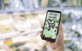 online shopping mobile app holding by a hand with blurred background of supermarket grocery on a mobile screen