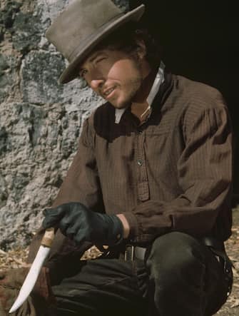 1973:  American folk rock singer and songwriter Bob Dylan wipes the blade of his dagger as he crouches in front of a doorway in a still from director Sam Peckinpah's film, 'Pat Garrett and Billy the Kid'.  (Photo by Fotos International/Getty Images)
