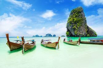 Longtale boats at the Phuket beach with limestone rock on background in Thailand.