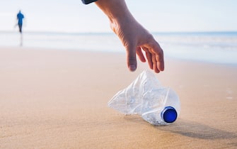 Hand picking up plastic bottle at beach.