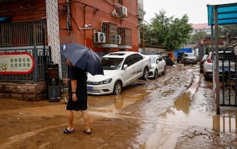 epa10779161 A man walks next to damaged by flood cars during a downpour in Mentougou District, west of Beijing, China, 01 August 2023. Heavy rains brought by Typhoon Doksuri caused floods in northern China and left two dead and thousands being evacuated as Beijing experienced its heaviest rainfall of the year.  EPA/MARK R. CRISTINO
