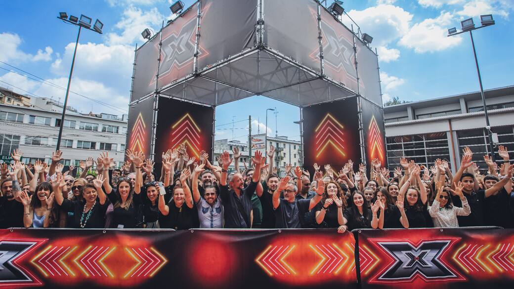 Una folla felice di persone aspetta di entrare come pubblico a X Factor