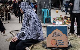 A Palestinian woman sits on a cart next to a box of food rations provided by US  charity World Central Kitchen at a makeshift street market in Rafah in the southern Gaza Strip on March 14, 2024, amid ongoing battles between Israel and the militant group Hamas. (Photo by MOHAMMED ABED / AFP)
