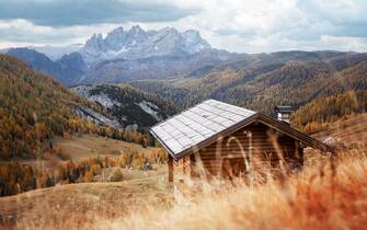 Incredible autumn view at Valfreda valley in Italian Dolomite Alps. Wooden cabin, yellow grass, orange larches forest and snowy mountains peaks on background. Dolomites, Italy. Landscape photography