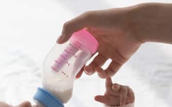 Young mom feeding sweet infant baby, giving formula