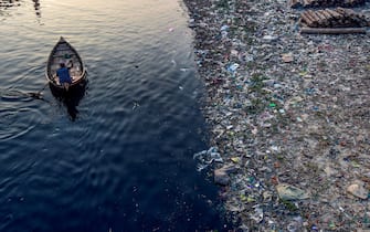 TOPSHOT - A man paddles on a boat as plastic bags float on the water surface of the Buriganga river in Dhaka on January 21, 2020. - Bangladesh's high court has ordered the shutdown of 231 factories that have contributed to Dhaka's main river becoming one of the world's most polluted, a lawyer said on January 21. (Photo by MUNIR UZ ZAMAN / AFP) (Photo by MUNIR UZ ZAMAN/AFP via Getty Images)