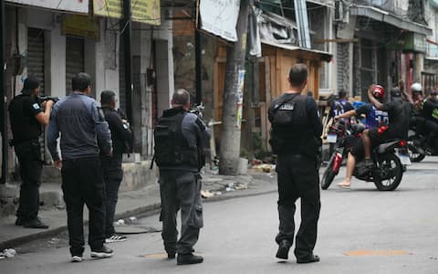 Police officer signal bikers to reverse during the Operacao Contencao (Operation Containment) at the Vila Cruzeiro favela, in the Penha complex, in Rio de Janeiro, Brazil, on October 28, 2025. At least 2,500 security forces agents took part in an operation to arrest drug traffickers from the Comando Vermelho (CV), which resulted in 18 suspects and several police officers dead. (Photo by Mauro PIMENTEL / AFP)