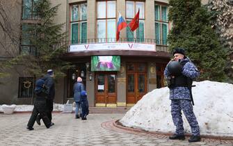 A police officer talks on phone as people arrive at a polling station to vote in Russia's presidential election in Moscow on March 17, 2024. (Photo by STRINGER / AFP)