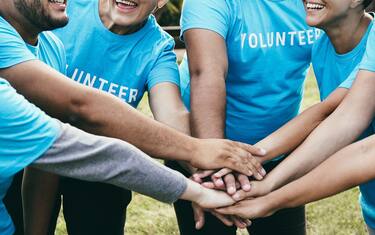 Happy group of volunteer people stacking hands celebrating together outdoor - Teamwork and charity support concept - Focus on back faces