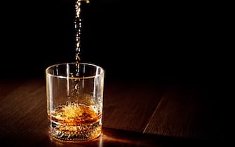 Scotch or bourbon whiskey (or whisky) being poured into a glass with dramatic studio lighting and a black background.