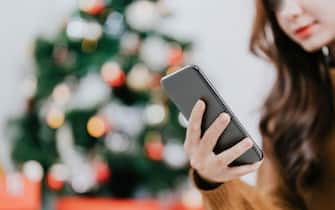Close up hand of woman using her Mobile Phone at home. Boke christmas tree background