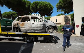 A Police officer walks past a burnt car being moved on the bed of a towing vehicle in the seaside resort of La Grande Motte, near the city of Montpellier, southern France, on August 26, 2024, following the August 24, 2024 attack to the Beth Yaacov synagogue. Two vehicles were set on fire near the Beth Yaacov synagogue in La Grande-Motte, a seaside resort near Montpellier, on August 24, 2024, explained the French National Anti-Terrorist Prosecutor's Office, as well as two additional fires which targeted two of the building's access doors. After being on the run for fifteen hours, the suspected attacker of the synagogue was arrested in NÃ®mes, on August 24, 2024. (Photo by Pascal GUYOT / AFP) (Photo by PASCAL GUYOT/AFP via Getty Images)